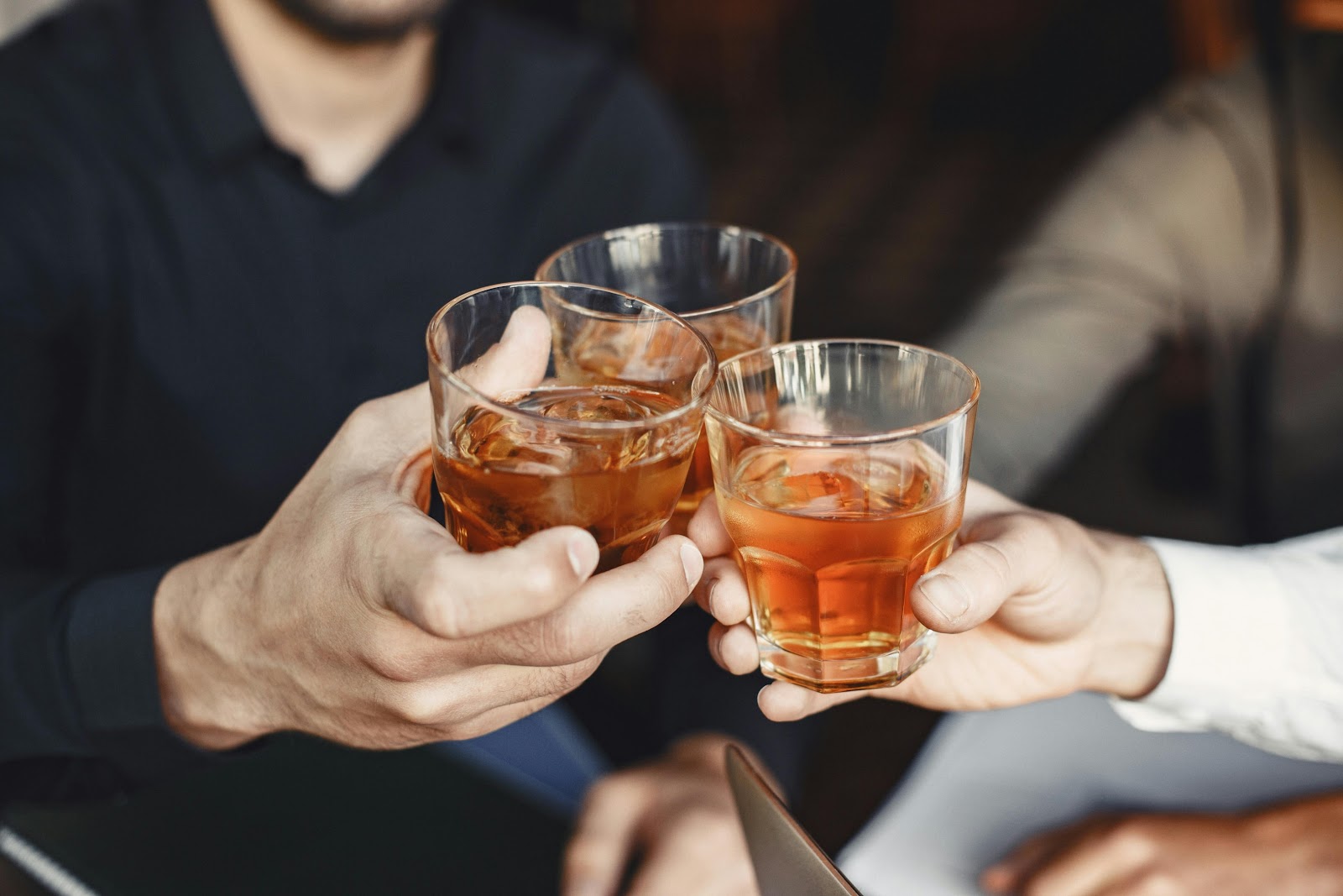 A close-up of three people raising glasses filled with an amber-colored drink and ice.